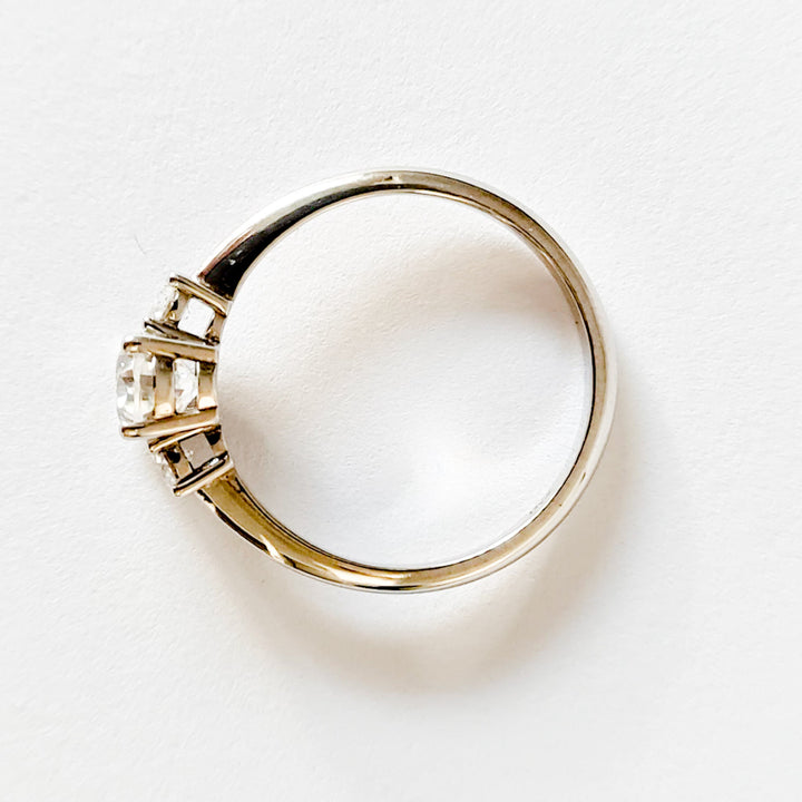 Oval and round cut moissanite three stone engagement ring in white gold, top view on white background