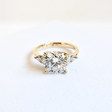 Cushion and pear cut moissanite three stone engagement ring in white gold, front view on white background