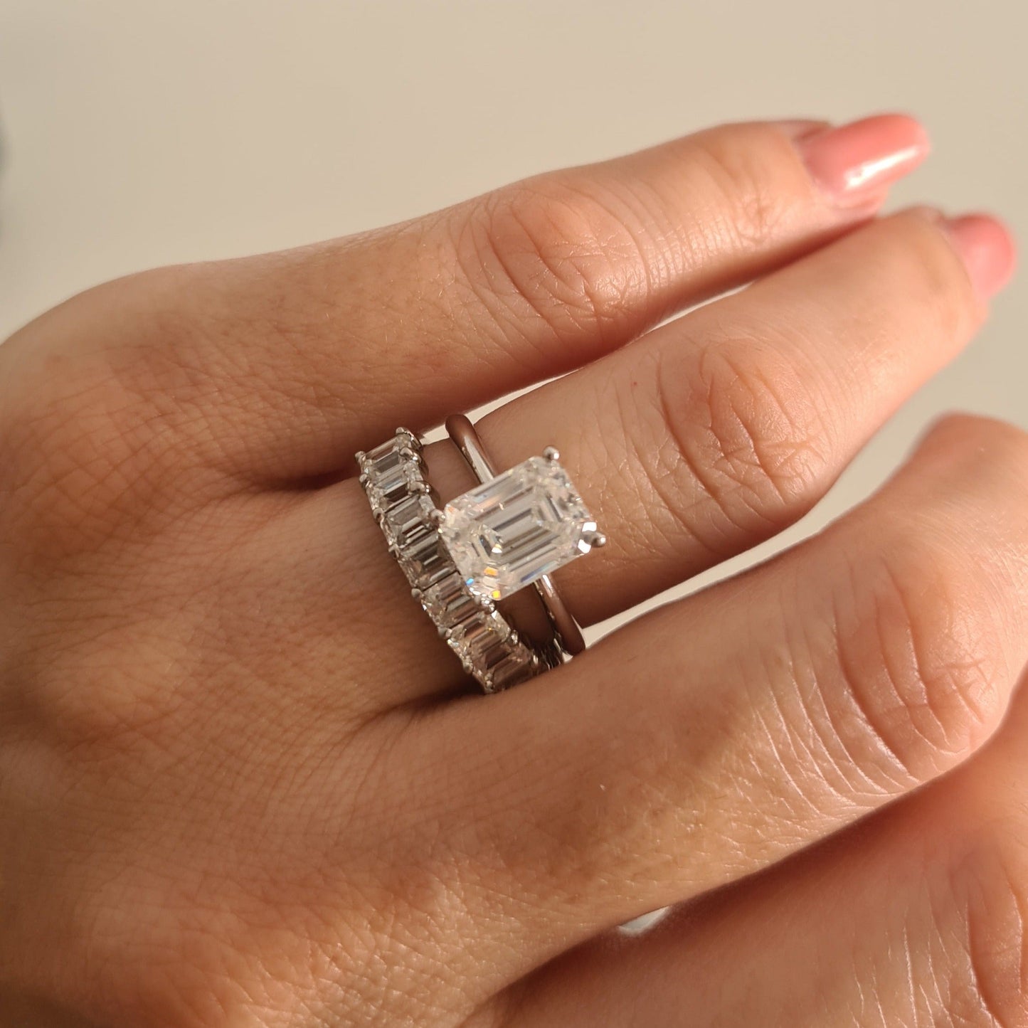 Ursa emerald cut moissanite engagement ring next to an eternity wedding band