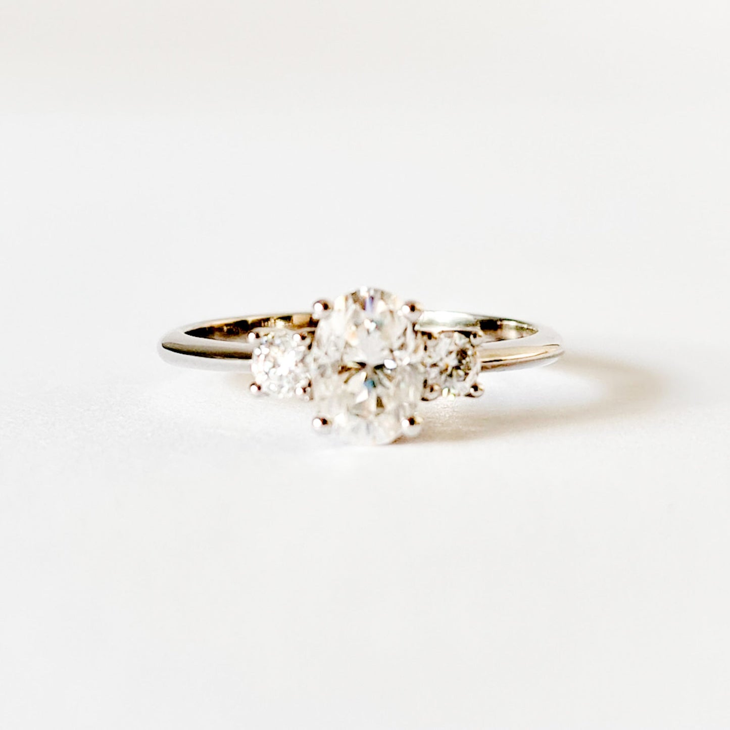 Oval and round cut moissanite three stone engagement ring in white gold, front view on white background