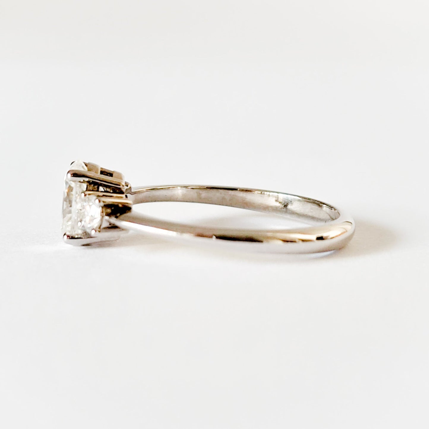 Oval and round cut moissanite three stone engagement ring in white gold, side view on white background