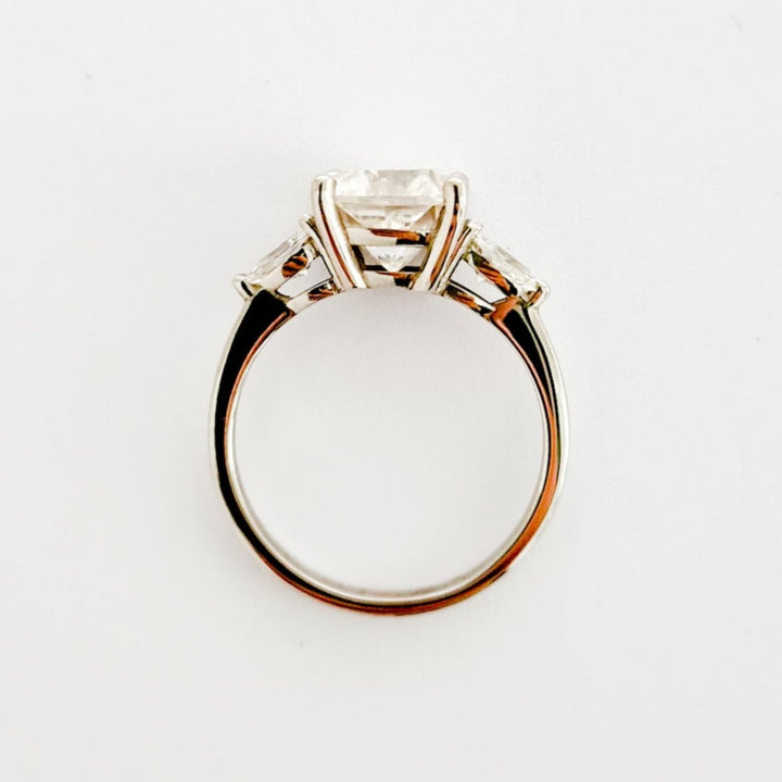 Cushion and pear cut moissanite three stone engagement ring in white gold, side view  on white background