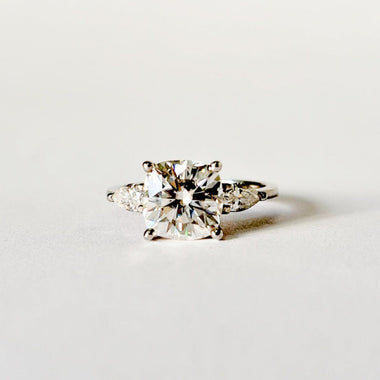 Cushion and pear cut moissanite three stone engagement ring in white gold, front view on white background