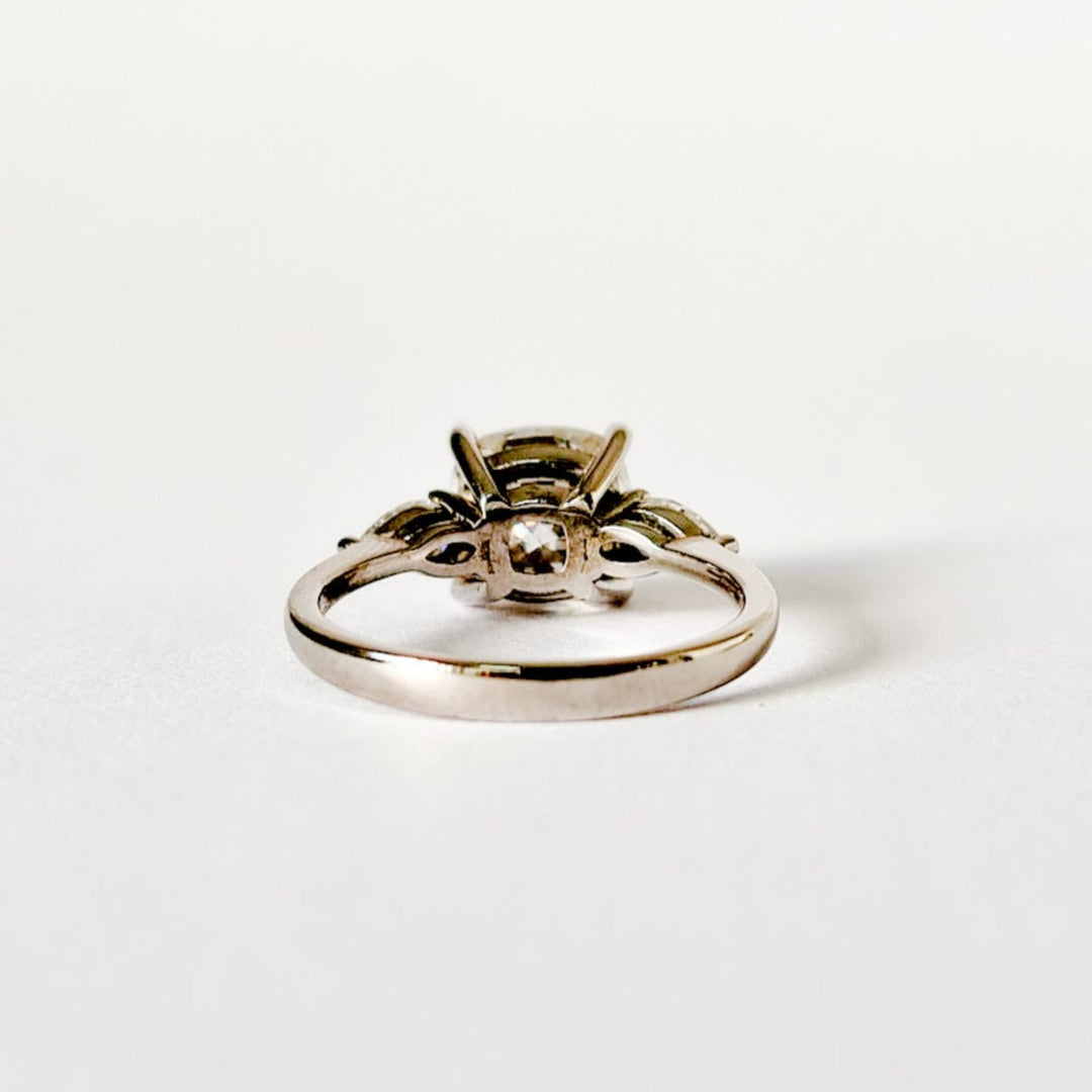 Cushion and pear cut moissanite three stone engagement ring in white gold, back view  on white background
