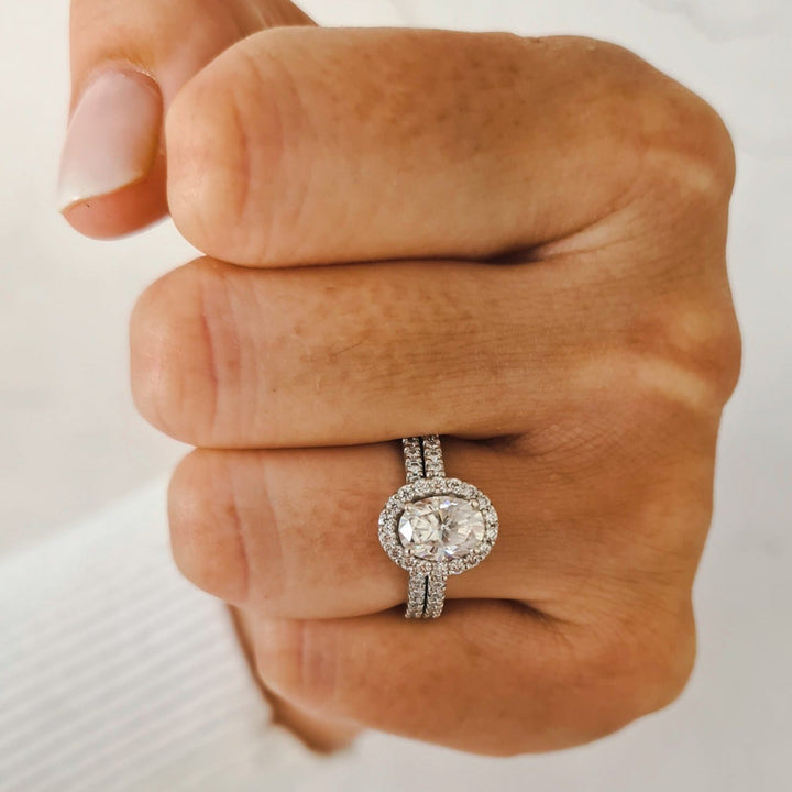 1.5 carat oval halo moissanite engagement ring set in platinum next to wedding band seen on hand for size comparison