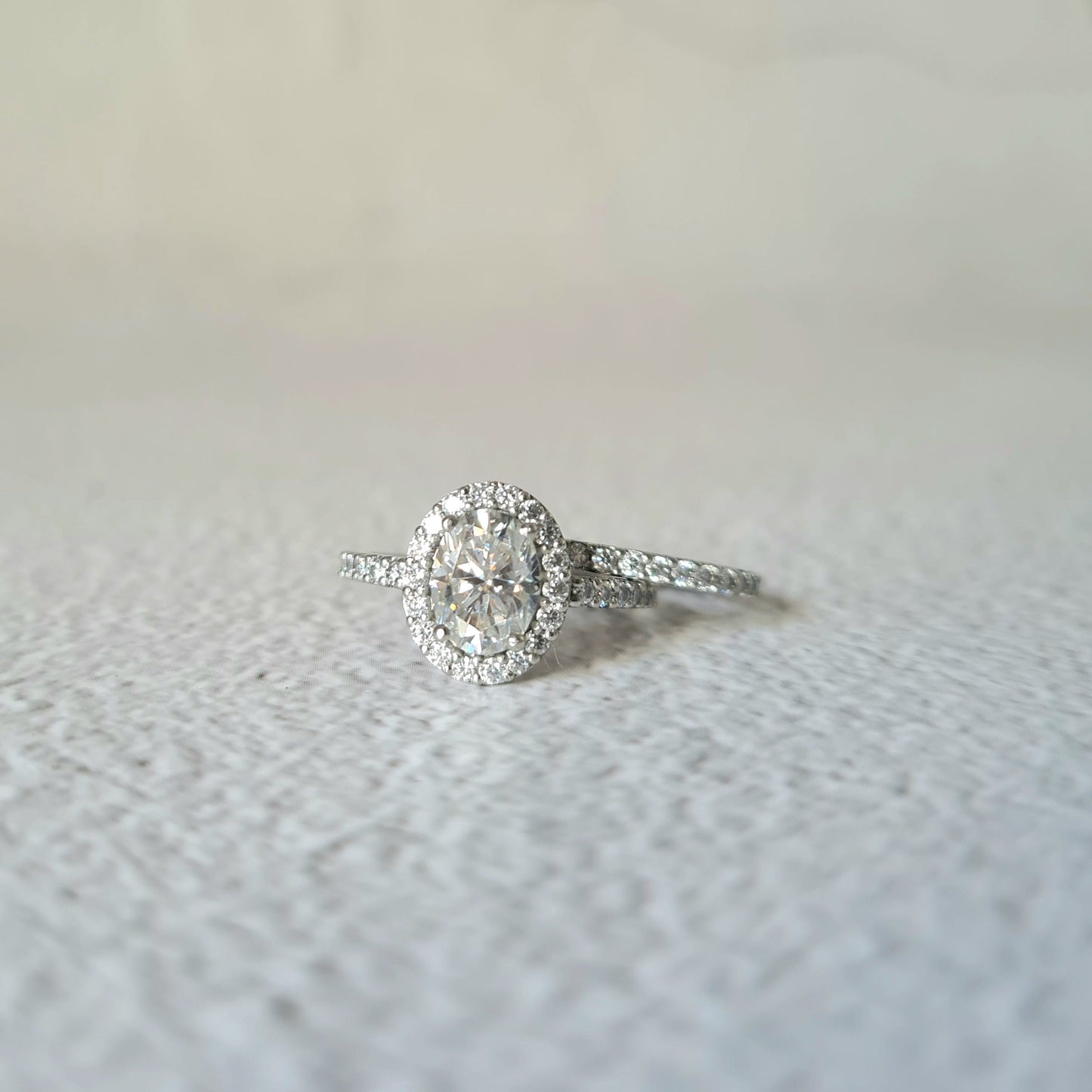 1.5 carat oval halo moissanite engagement ring set in platinum next to eternity wedding band