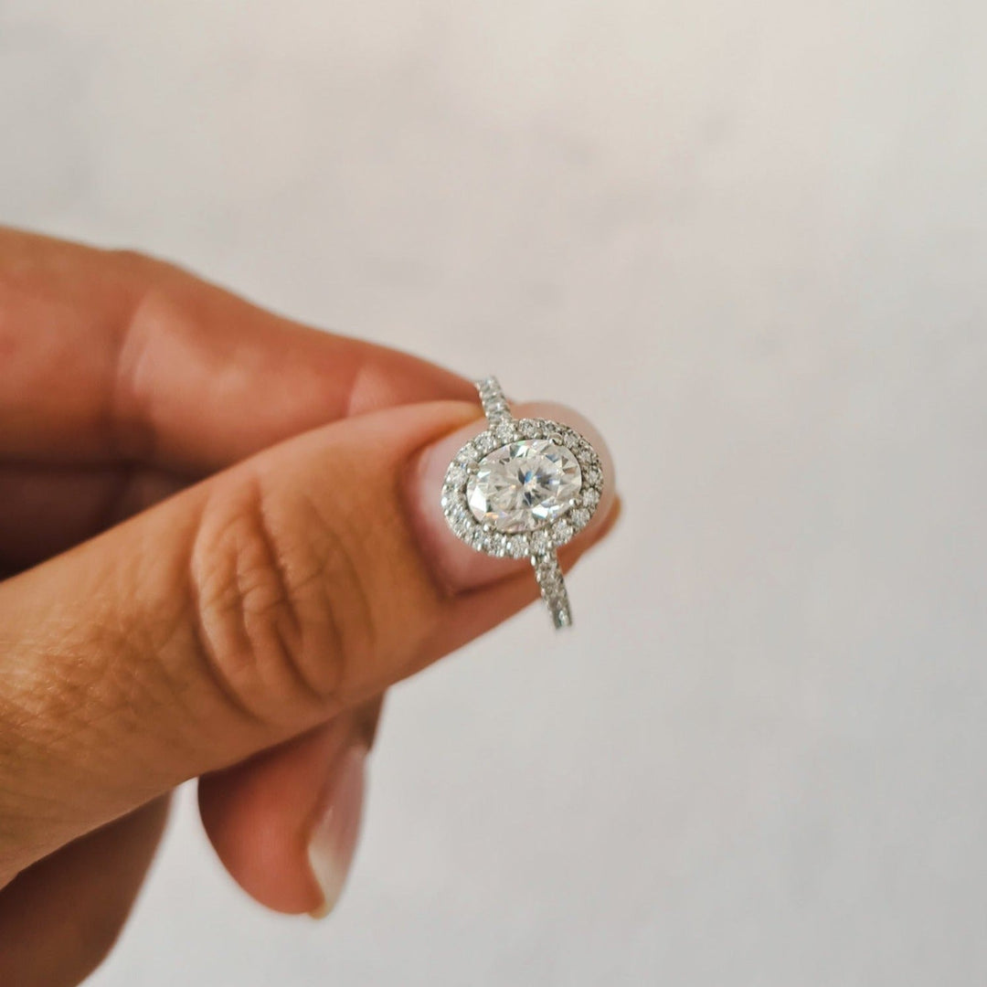 1.5 carat oval halo moissanite engagement ring set in platinum held between fingers for size reference