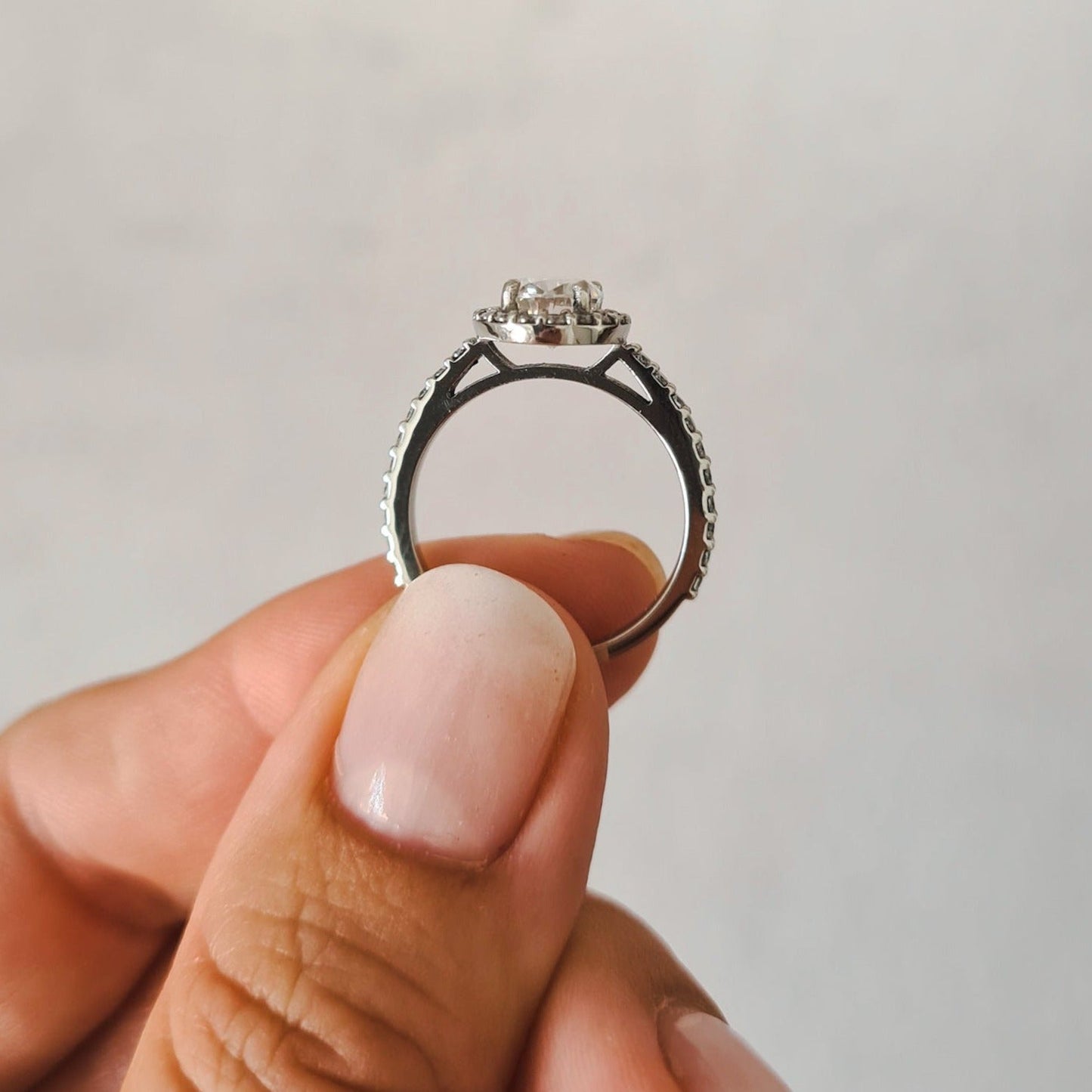 1.5 carat oval halo moissanite engagement ring set in platinum held between fingers for size reference