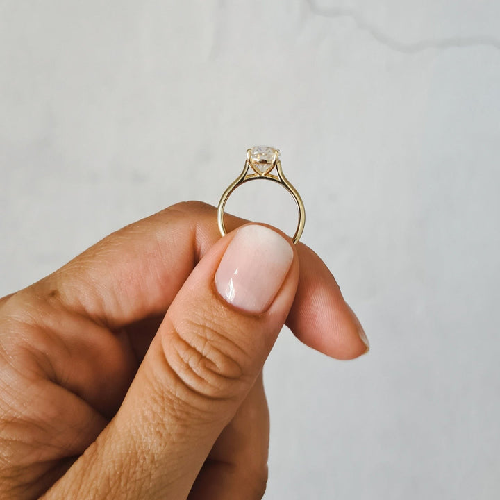 2ct oval moissanite solitaire engagement ring in 9ct yellow gold held between two fingers for size comparison