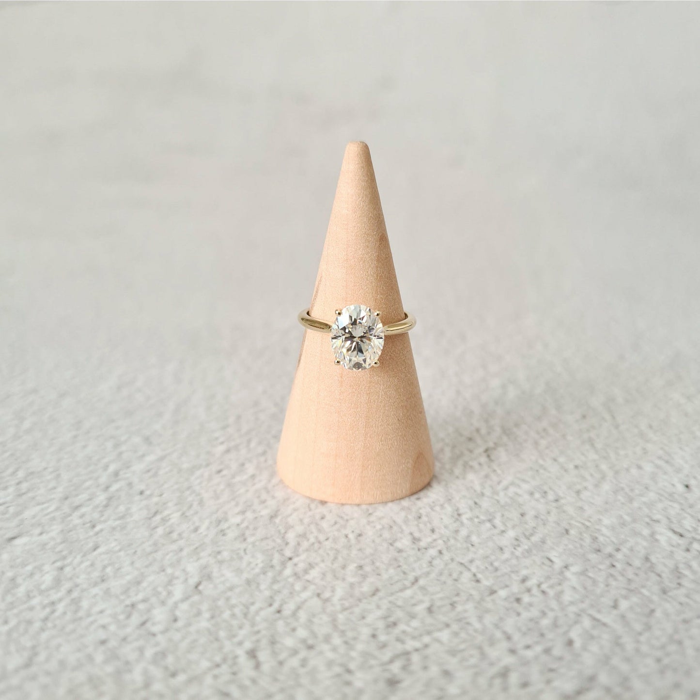 2ct oval moissanite solitaire engagement ring in 9ct yellow gold on a wood cone and grey background