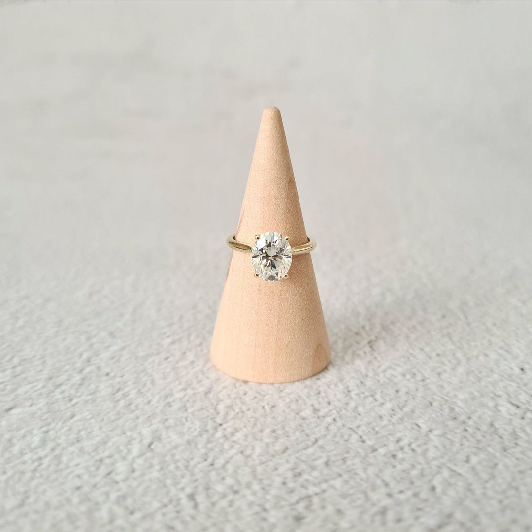 2ct oval moissanite solitaire engagement ring in 9ct yellow gold on a wood cone and grey background